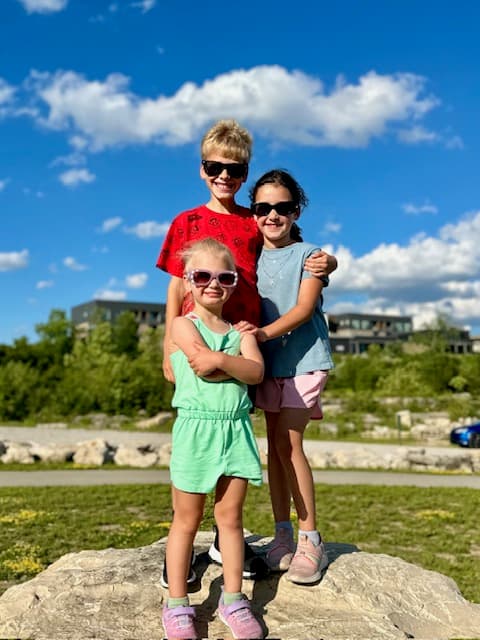 Three children standing together outside under a blue sky